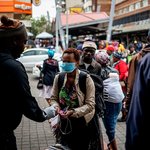 A taxi rank marshal sprays hand sanitiser on a commuter wearing a mask as a preventive measure as she arrives at the Wanderers taxi rank in Johannesburg. Marco Longari/AFP via Getty Images